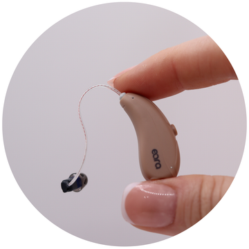 Eara self fitting otc Explore Li + hearing aids held between thumb and index finger, showing compact design of the hearing aid about the size of a paper clip which is 2.54cm