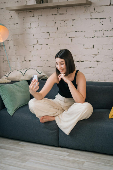 woman in black tank top taking a video call, sitting on a dark grey couch